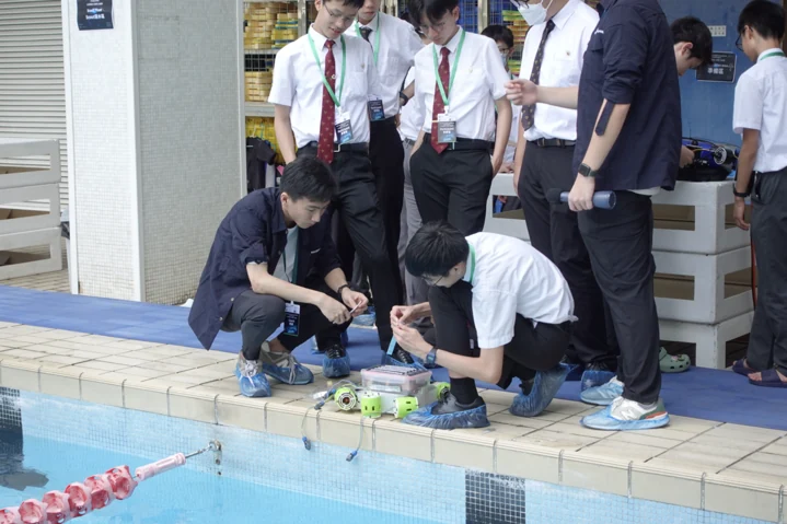 Students and a coach preparing their underwater robot beside the pool