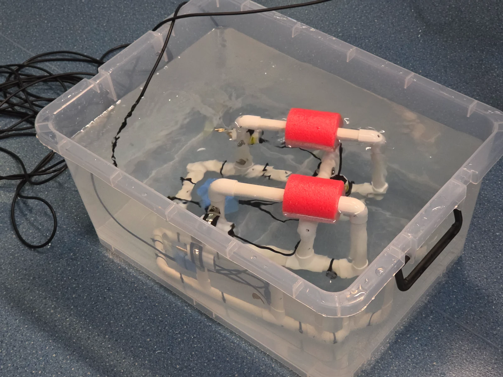 A white PVC underwater robot with red floats being tested in a clear water tank