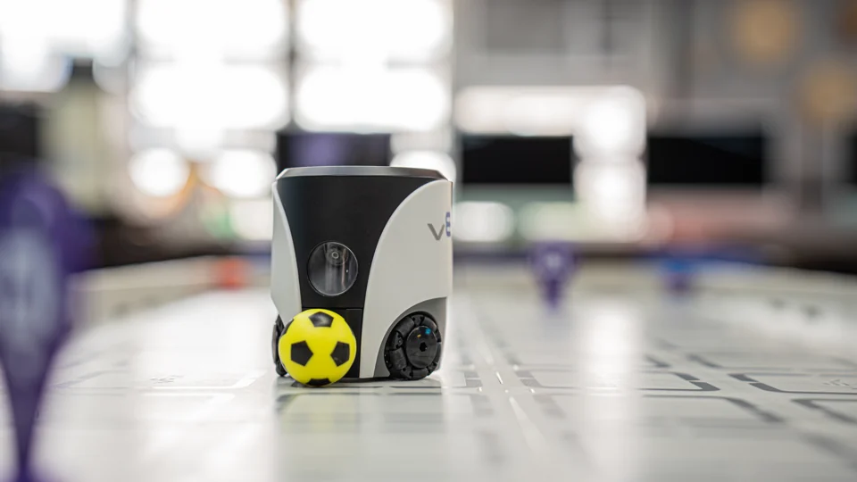 A VEX AIM robot with a yellow ball on a robotics activity mat